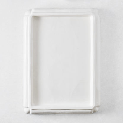 Rectangular white ceramic serving tray with a raised rim and decorative molded edges on a white background.