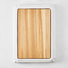 Rectangular oak wood cutting board set in a white ceramic serving base with handles.
