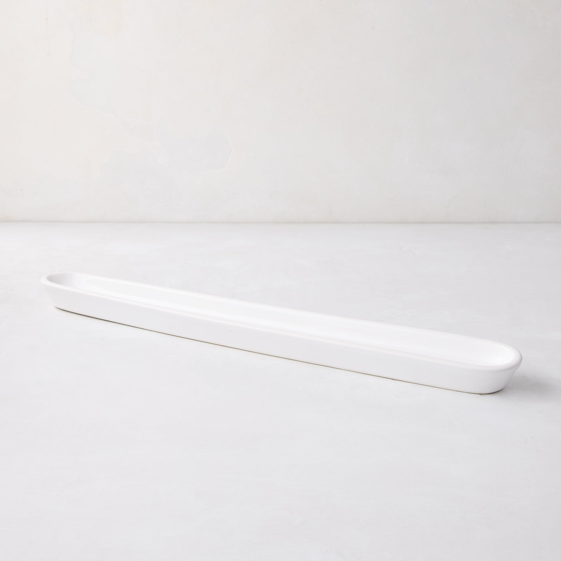 White ceramic olive serving tray, 16" long, with a narrow, rectangular shape and rounded ends.