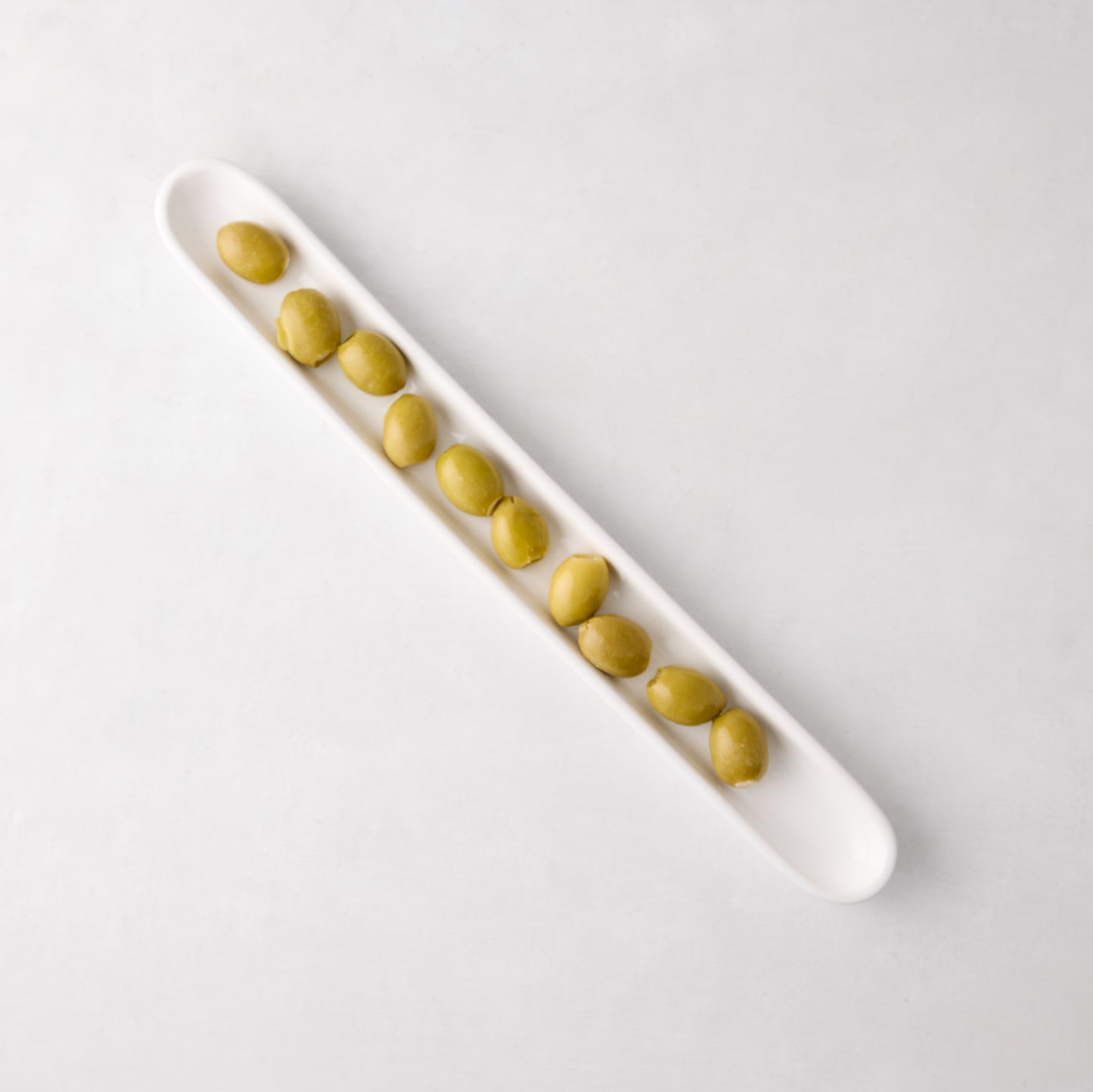 White ceramic olive serving tray, 16" long, filled with green olives.