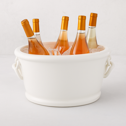 White ceramic oval ice bucket with ring handles, holding four bottles of rosé and white wine on ice.