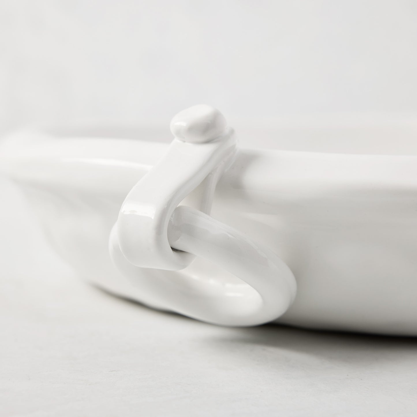 White ceramic oval platter with a ring handle and faux strap detail.