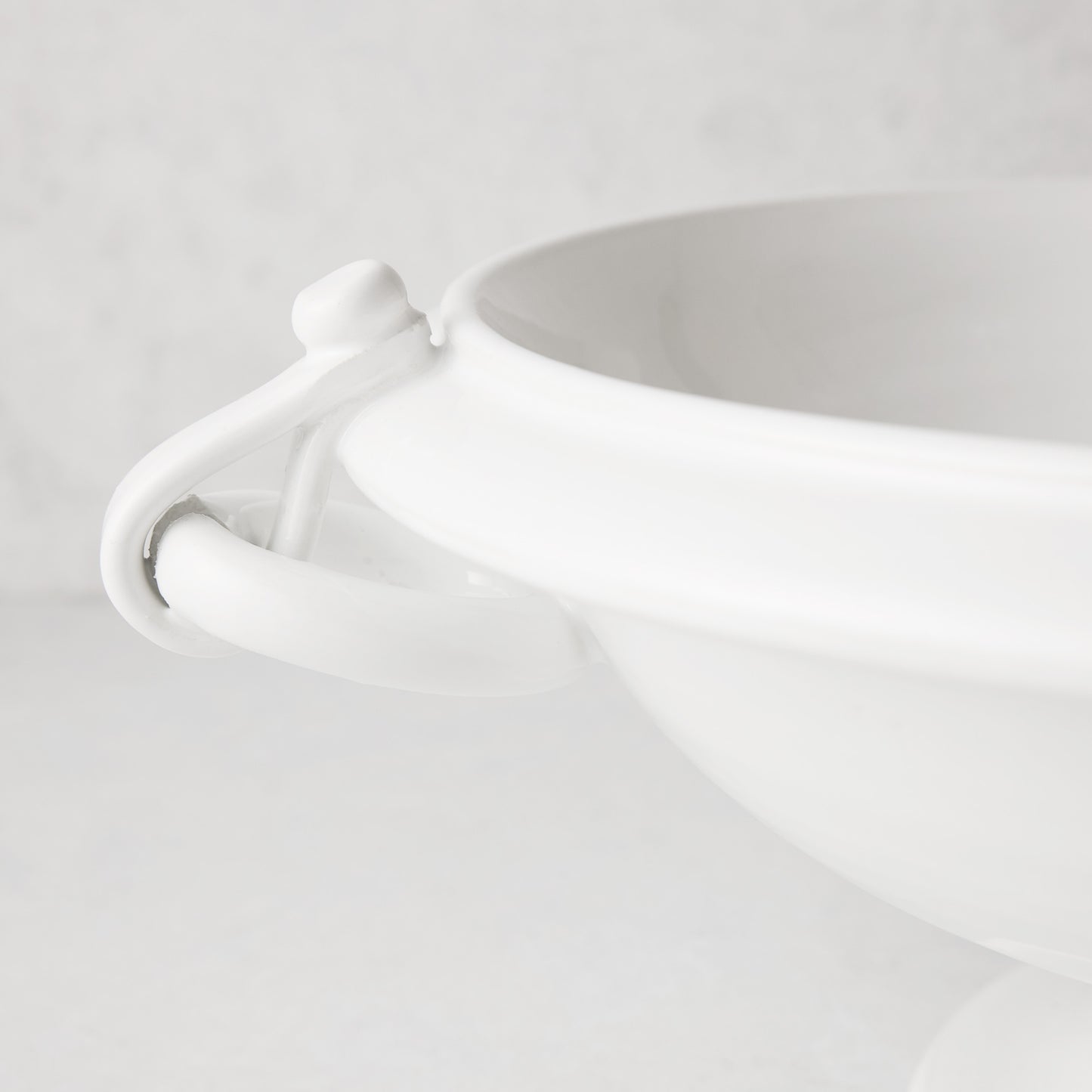 White ceramic pedestal fruit bowl with ring handle and faux straps.