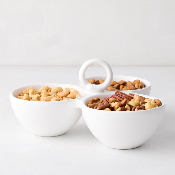 White ceramic triple serve bowl with handle, filled with cashews, almonds, and pecans.