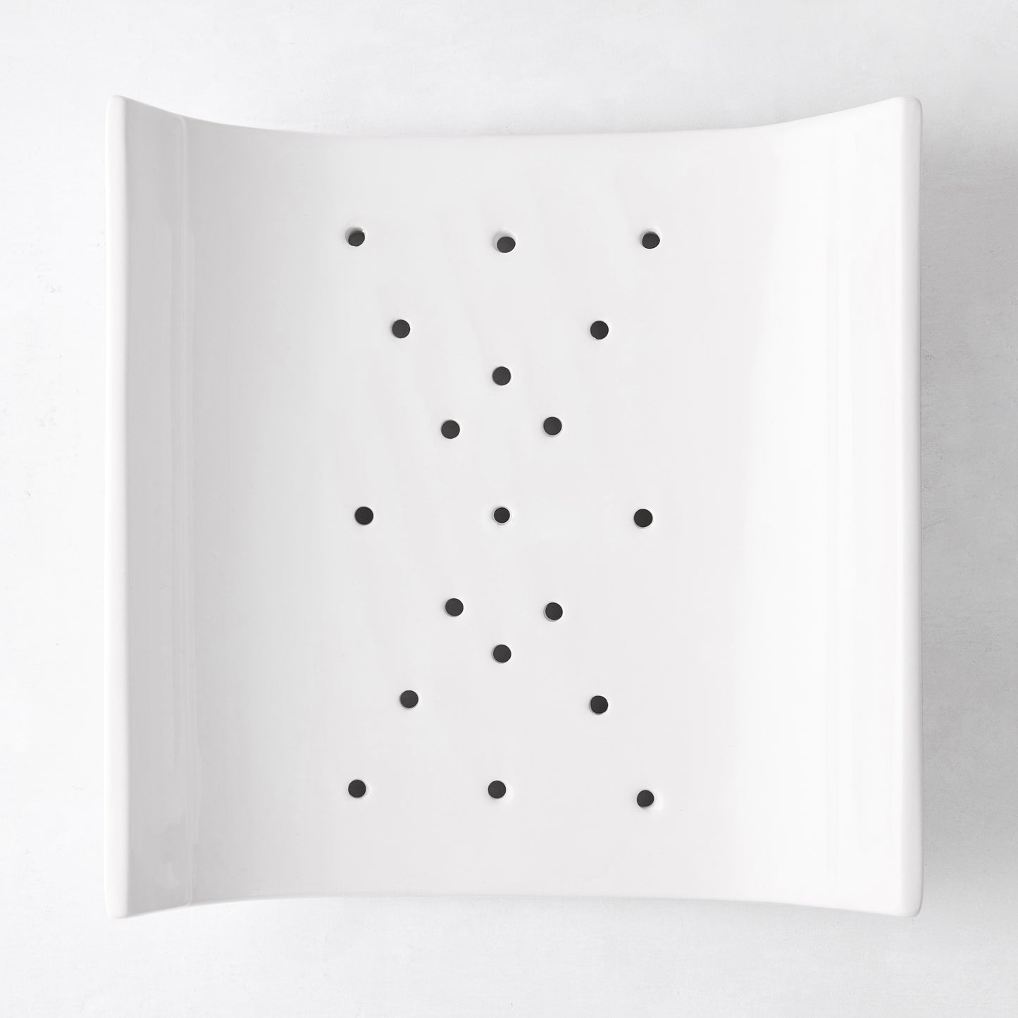 White ceramic vegetable drainer, square with rounded corners, open-ended design, small drainage holes.