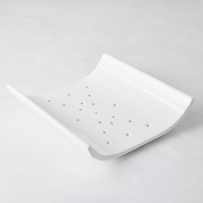 White ceramic vegetable drainer with an open-ended, curved design and drainage holes.