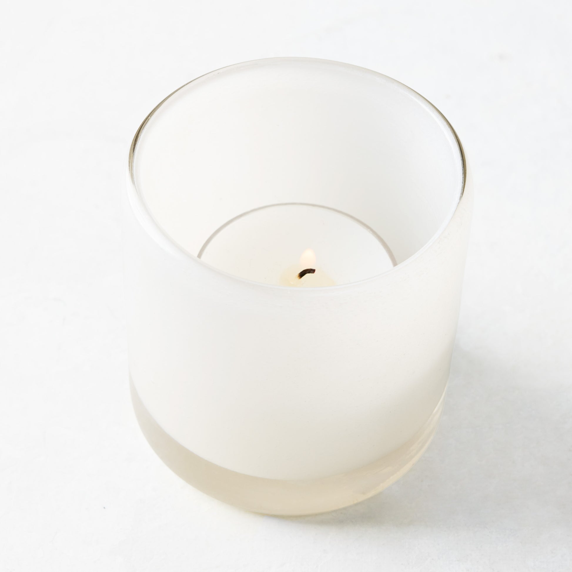 White glass votive candle holder with a lit tealight candle inside.