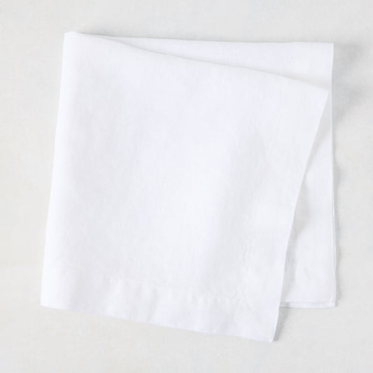 White HG Signature hand-dyed 22" square linen napkin, folded on a light surface.