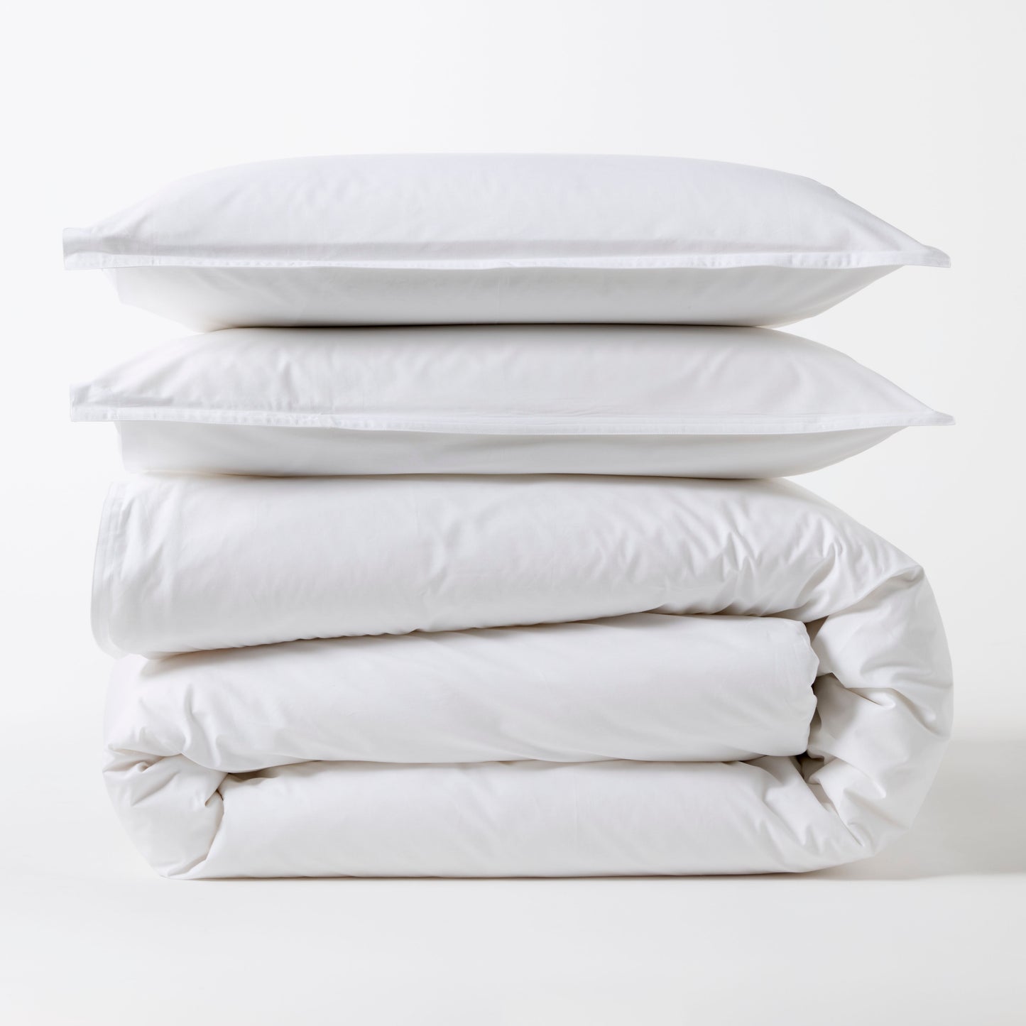 Stacked white Italian percale duvet set with two shams and a folded duvet cover.