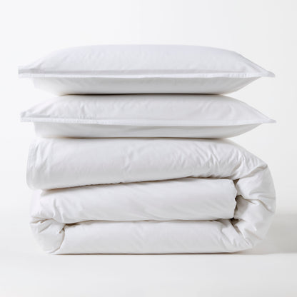 Stacked white Italian percale duvet set with two shams and a folded duvet cover.