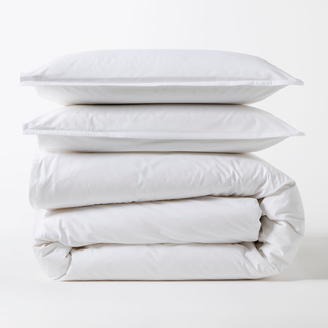 Stacked white Italian percale duvet set with two shams and a folded duvet cover.