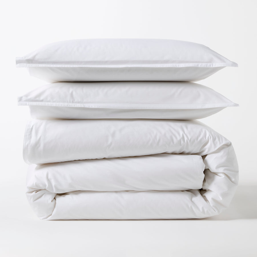 Stacked white Italian percale duvet set with two shams and a folded duvet cover.