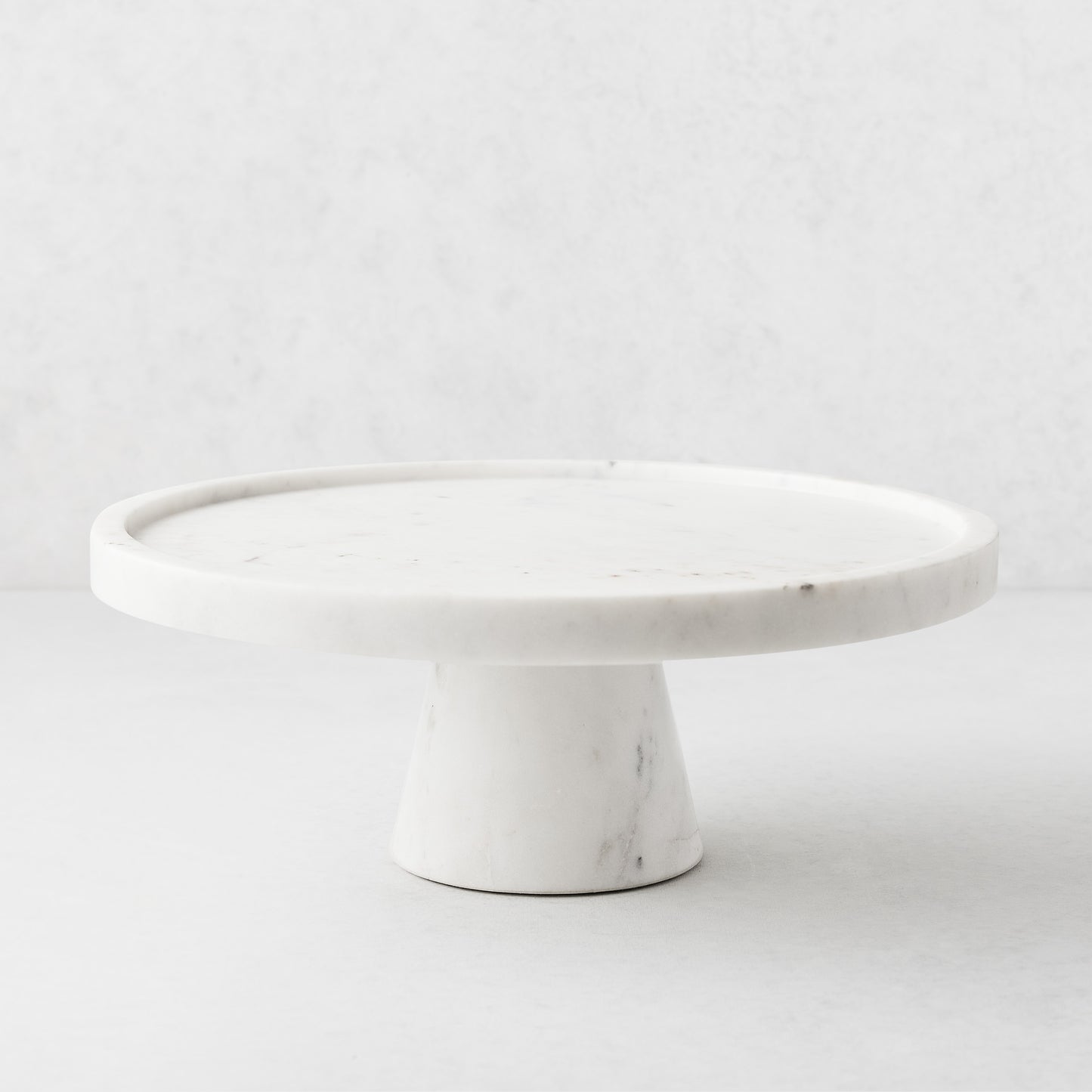 White marble cake stand, 12" diameter, with a raised lip and sturdy pedestal base.
