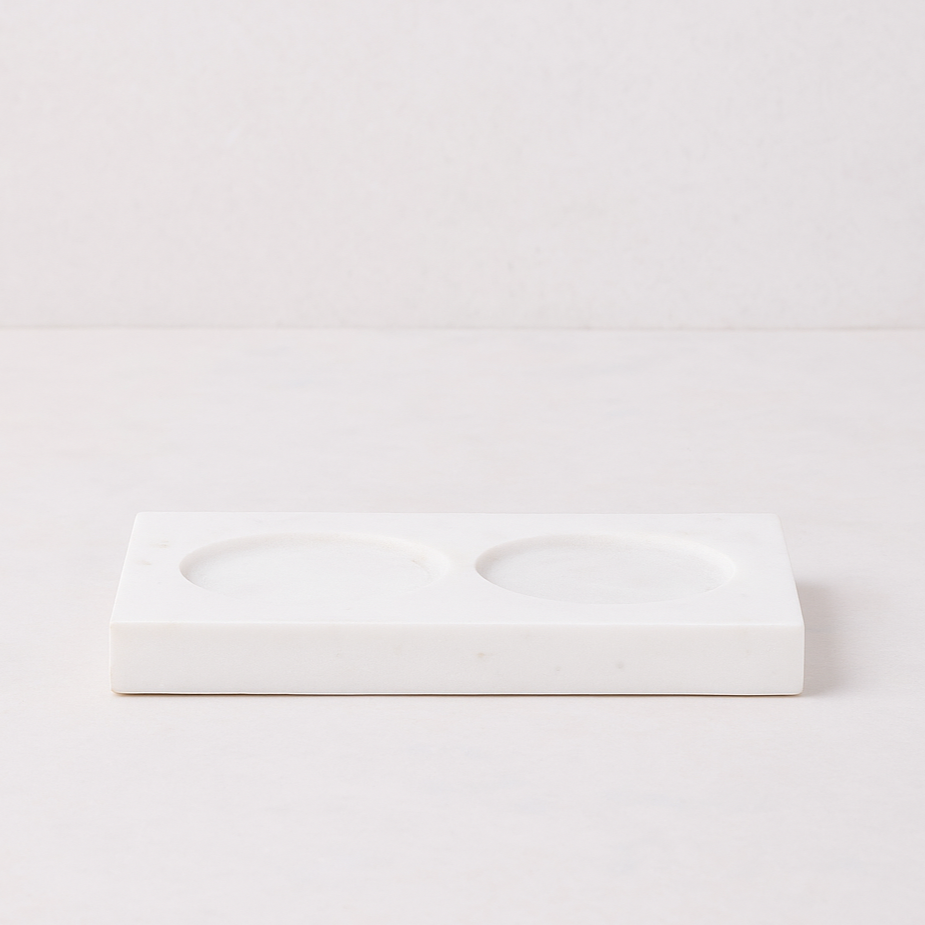 White marble rectangular tray with two circular indentations for dish soap and lotion bottles.