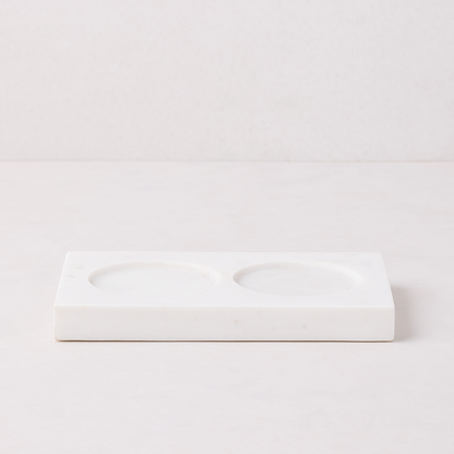 White marble rectangular tray with two circular indentations for dish soap and lotion bottles.