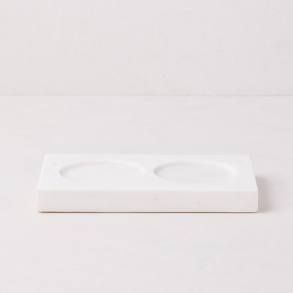 White marble rectangular tray with two circular indentations for soap and lotion bottles.