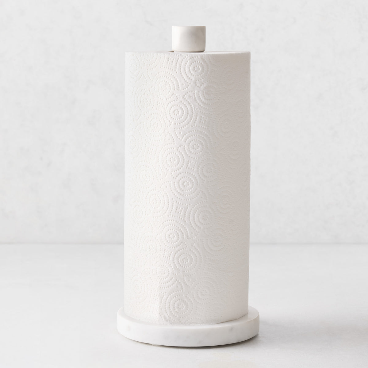 White marble paper towel holder with a heavy round base and sleek pole, holding a roll of white paper towels.