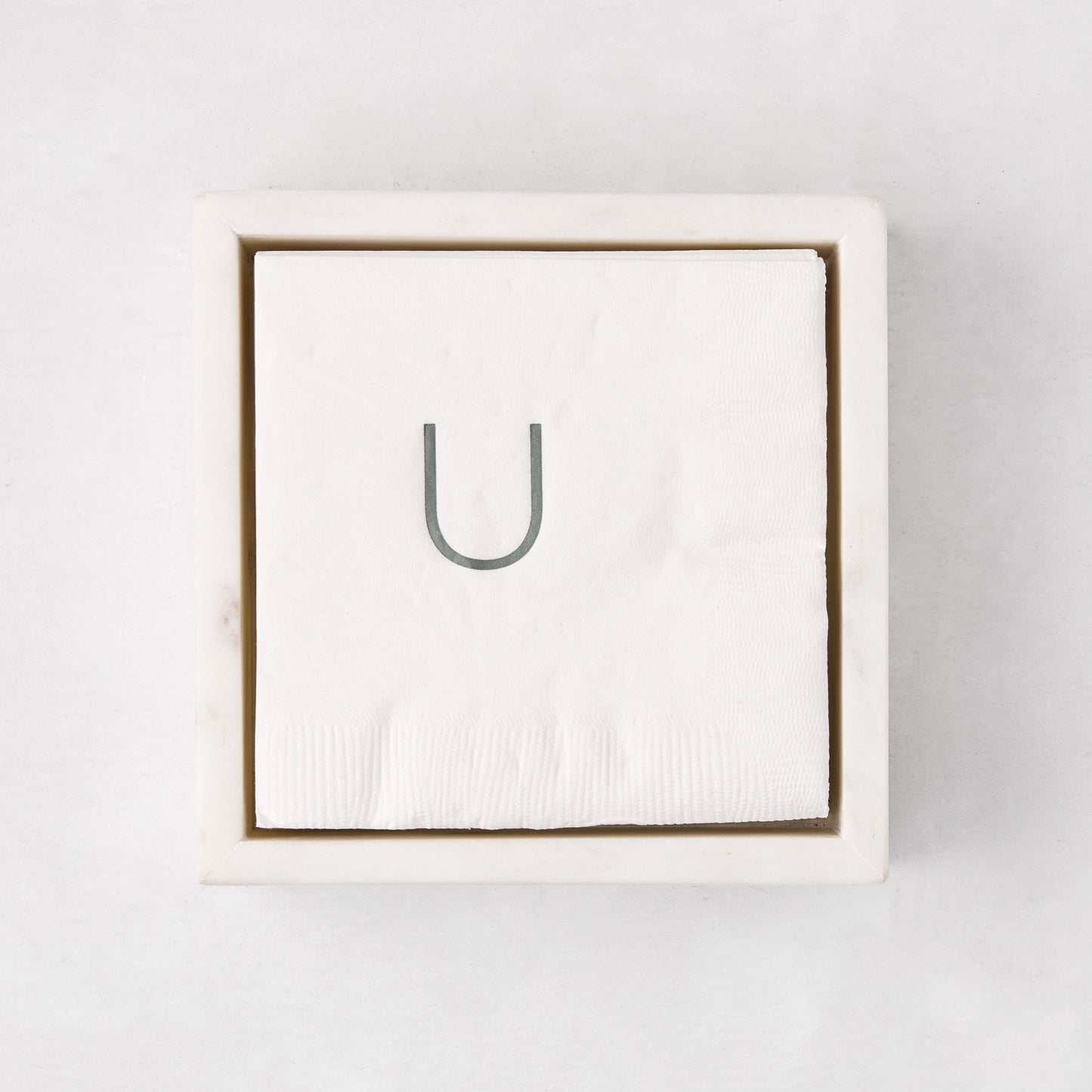 White marble square napkin holder with a stack of white napkins, top-down view.