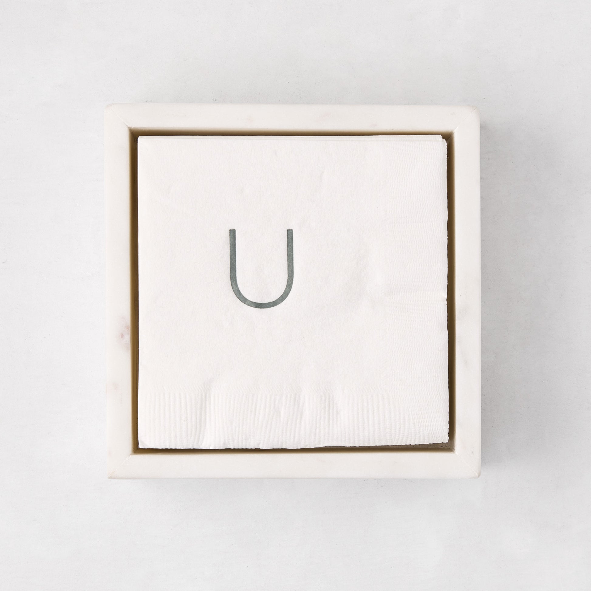 White marble square napkin holder with a stack of white napkins, top-down view.