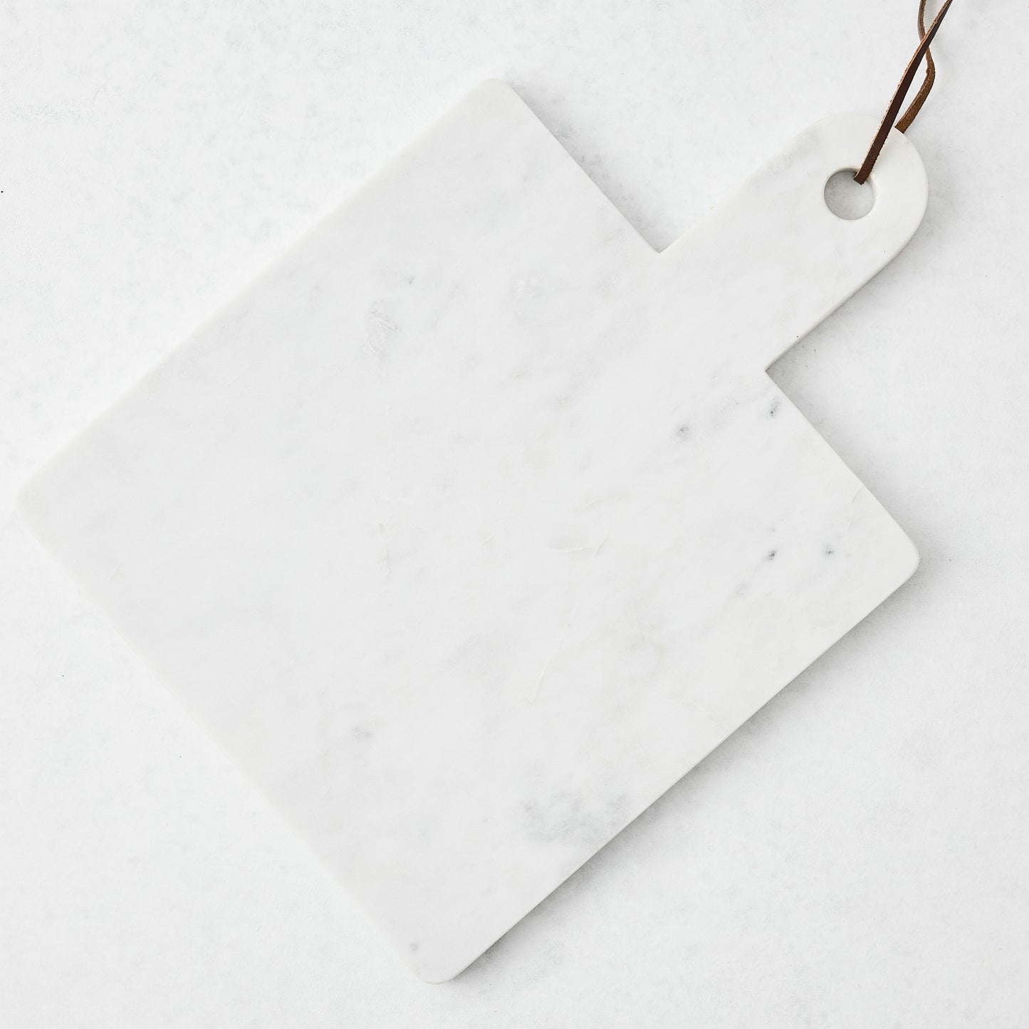White marble square serve board with handle and brown leather strap.