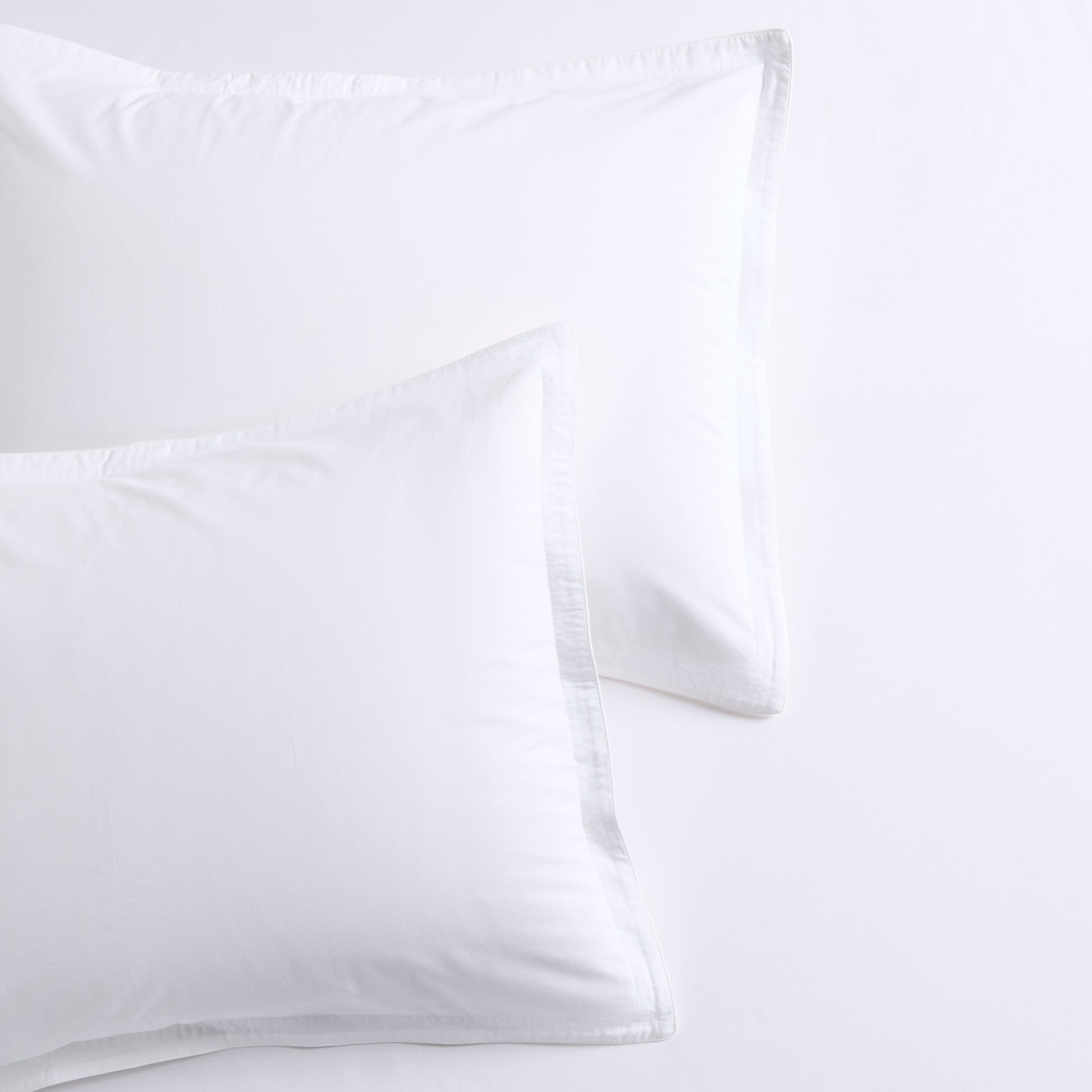 Two white percale pillow shams with delicate white piping and double-stitch detailing.