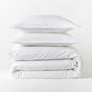 Stacked white piped percale duvet cover and two shams, 100% cotton, 310-thread-count.