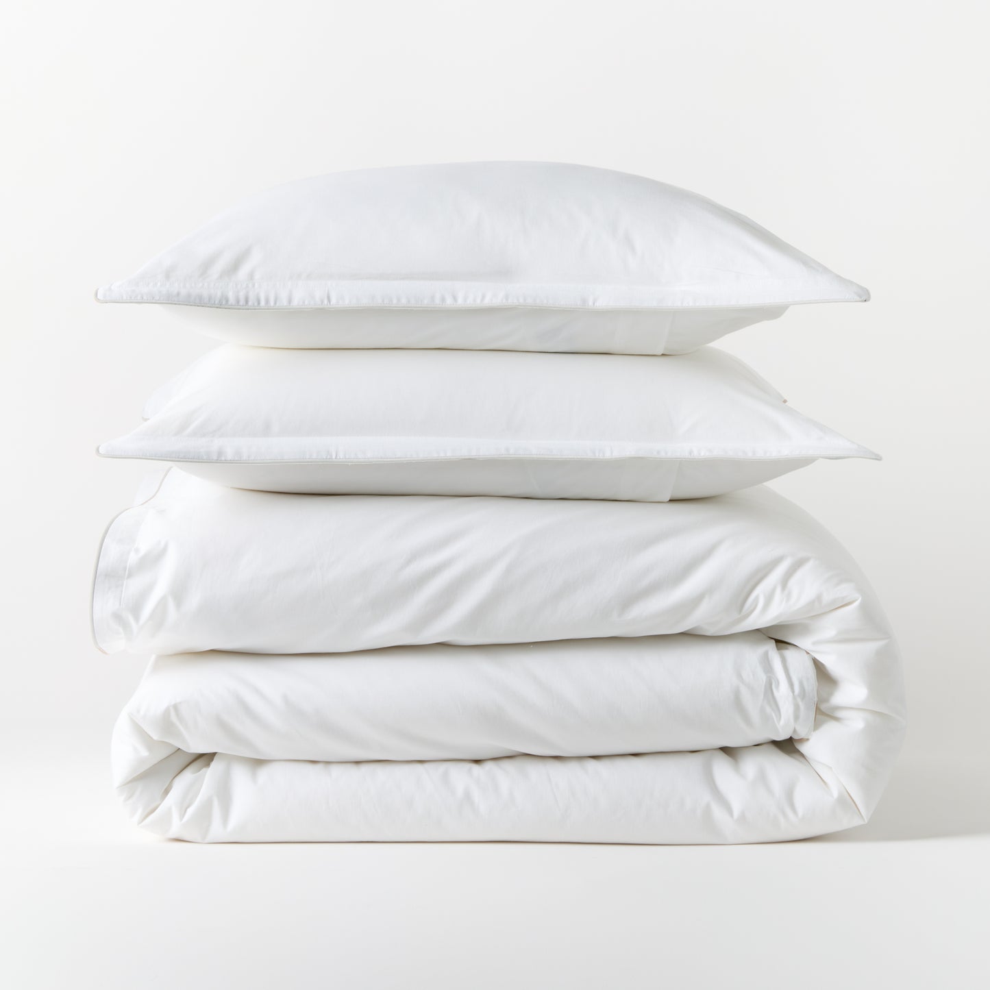 Stacked white piped percale duvet cover and two shams, 100% cotton, 310-thread-count.