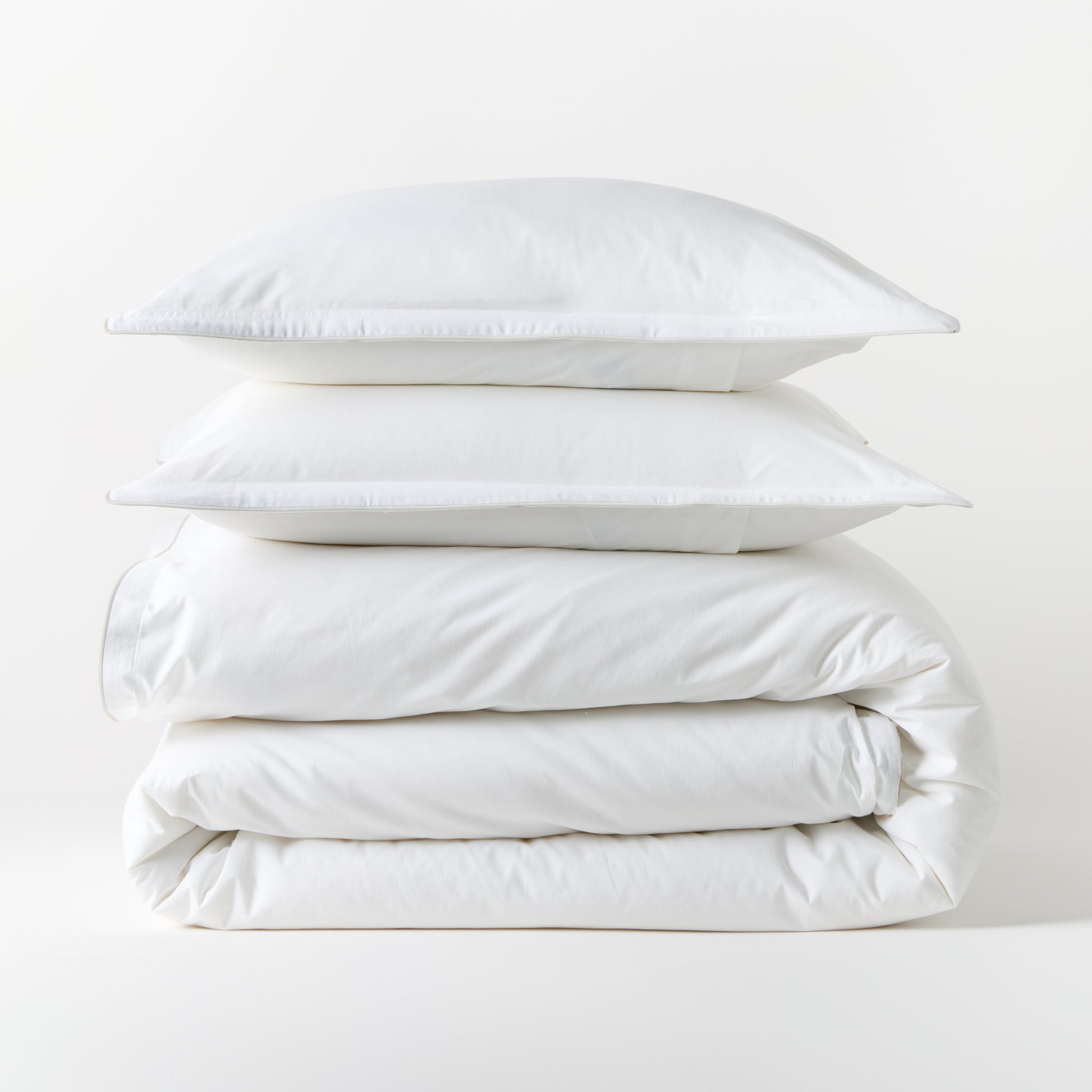 Stacked white piped percale duvet cover and two shams, 100% cotton, 310-thread-count.