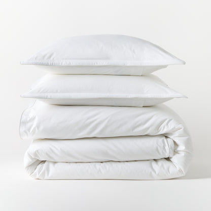 Stacked white piped percale duvet cover and two shams, 100% cotton, 310-thread-count.