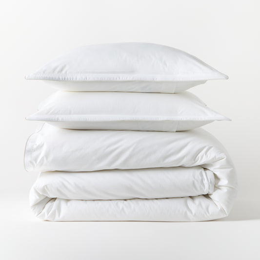 Stacked white piped percale duvet cover and two shams, 100% cotton, 310-thread-count.