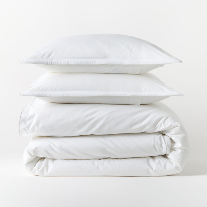 Stacked white piped percale duvet cover and two shams, 100% cotton, 310-thread-count.