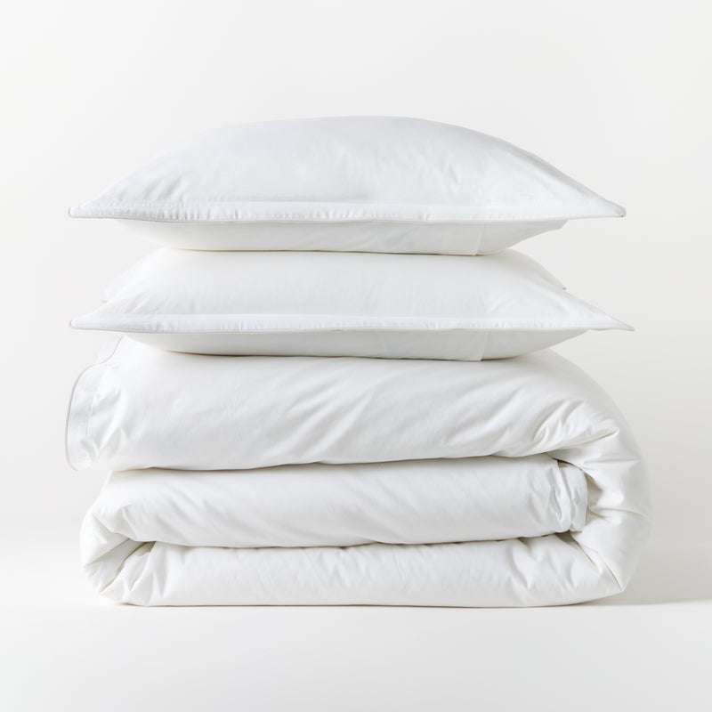 Stacked white piped percale duvet cover and two shams, 100% cotton, 310-thread-count.