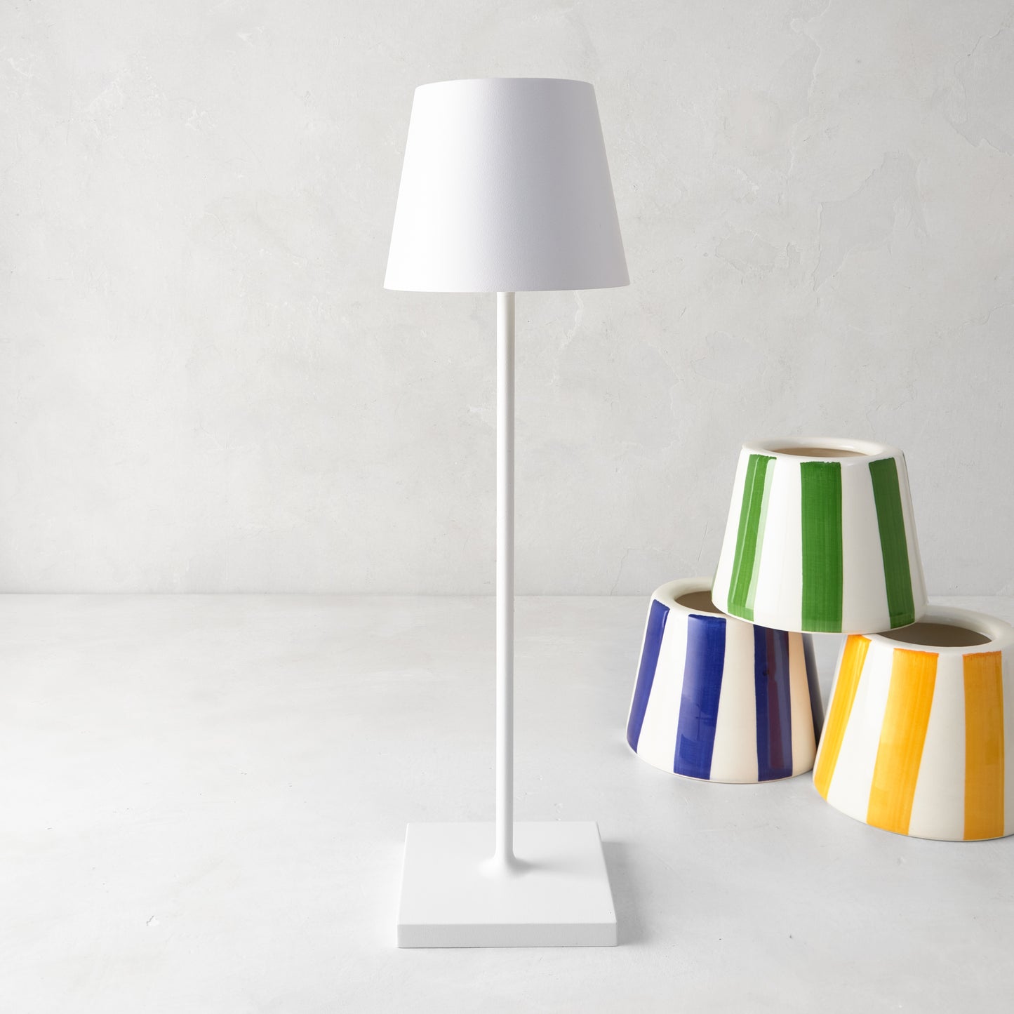 White Poldina rechargeable lamp with a sleek, modern design, standing next to colorful striped planters.