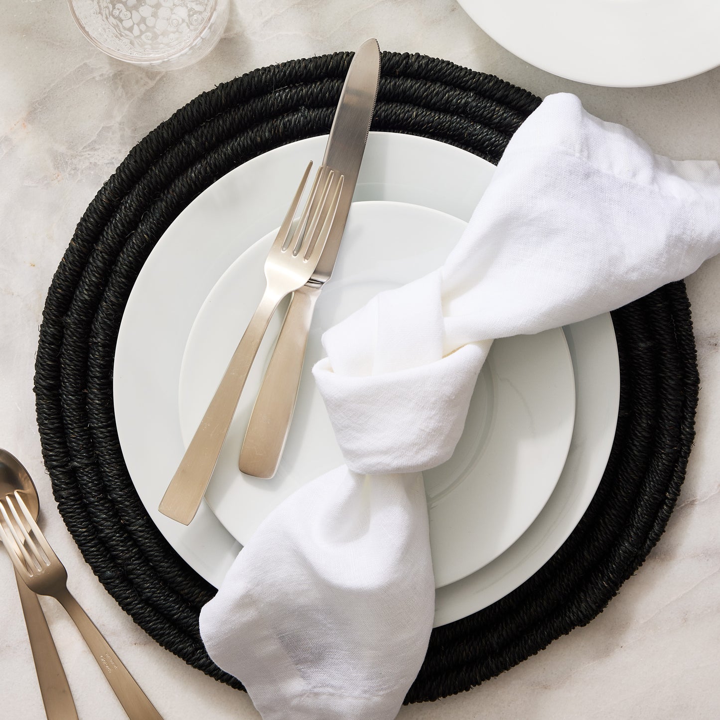 White HG Signature hand-dyed 22" square linen napkin, knotted on a white plate with cutlery.