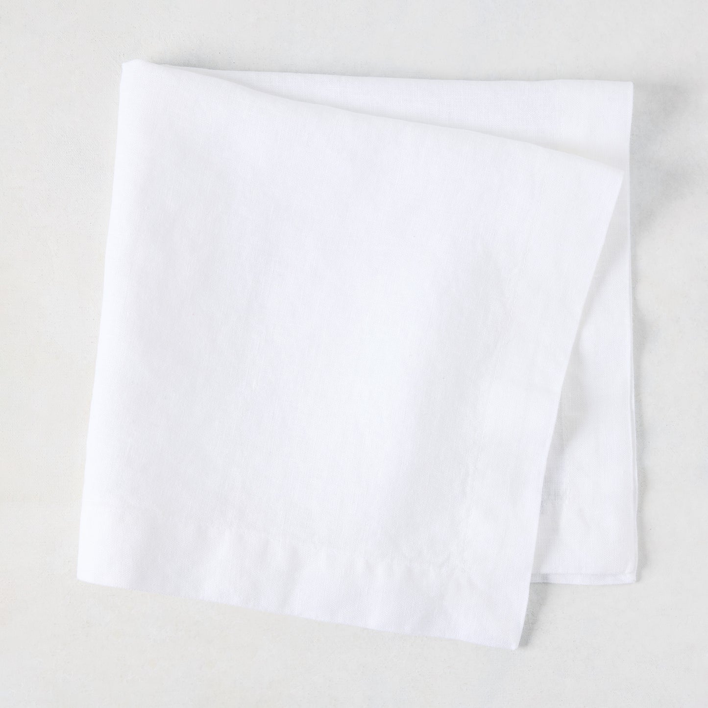White HG Signature hand-dyed 22" square linen napkin, folded on a light surface.
