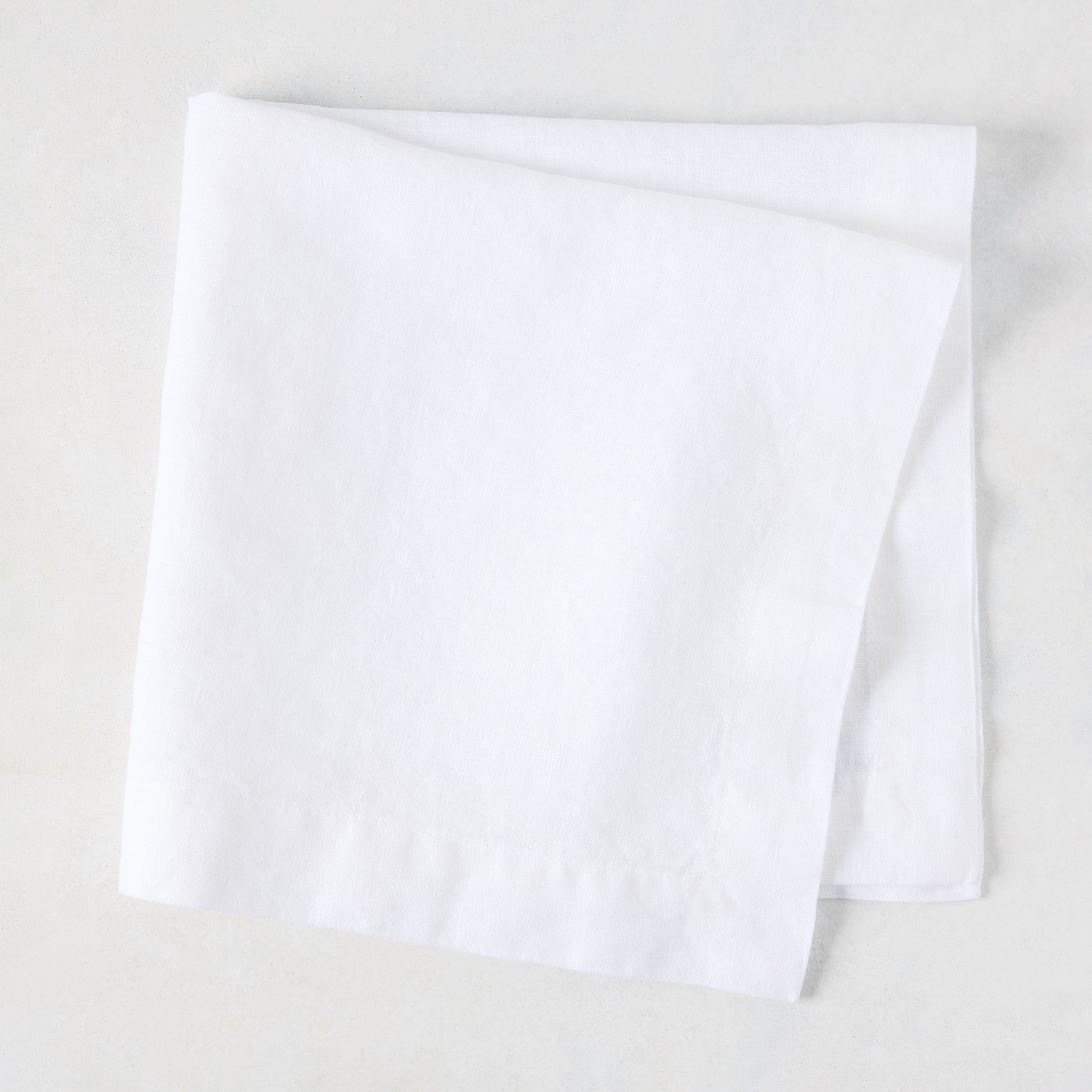 White HG Signature hand-dyed 22" square linen napkin, folded on a light surface.