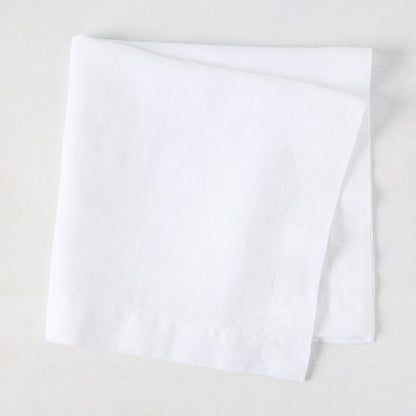 White HG Signature hand-dyed 22" square linen napkin, folded on a light surface.