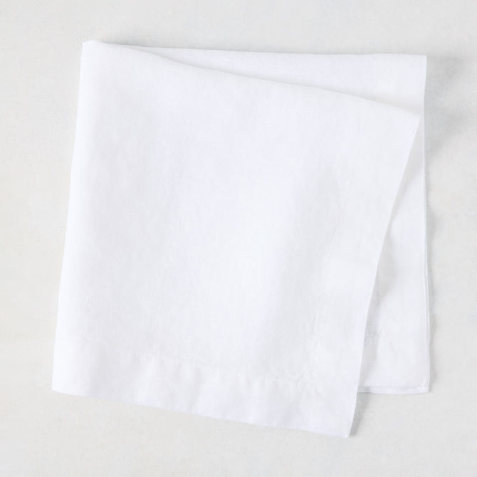 White HG Signature hand-dyed 22" square linen napkin, folded on a light surface.