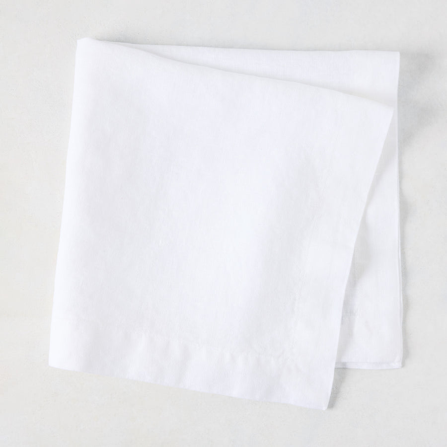 White HG Signature hand-dyed 22" square linen napkin, folded on a light surface.