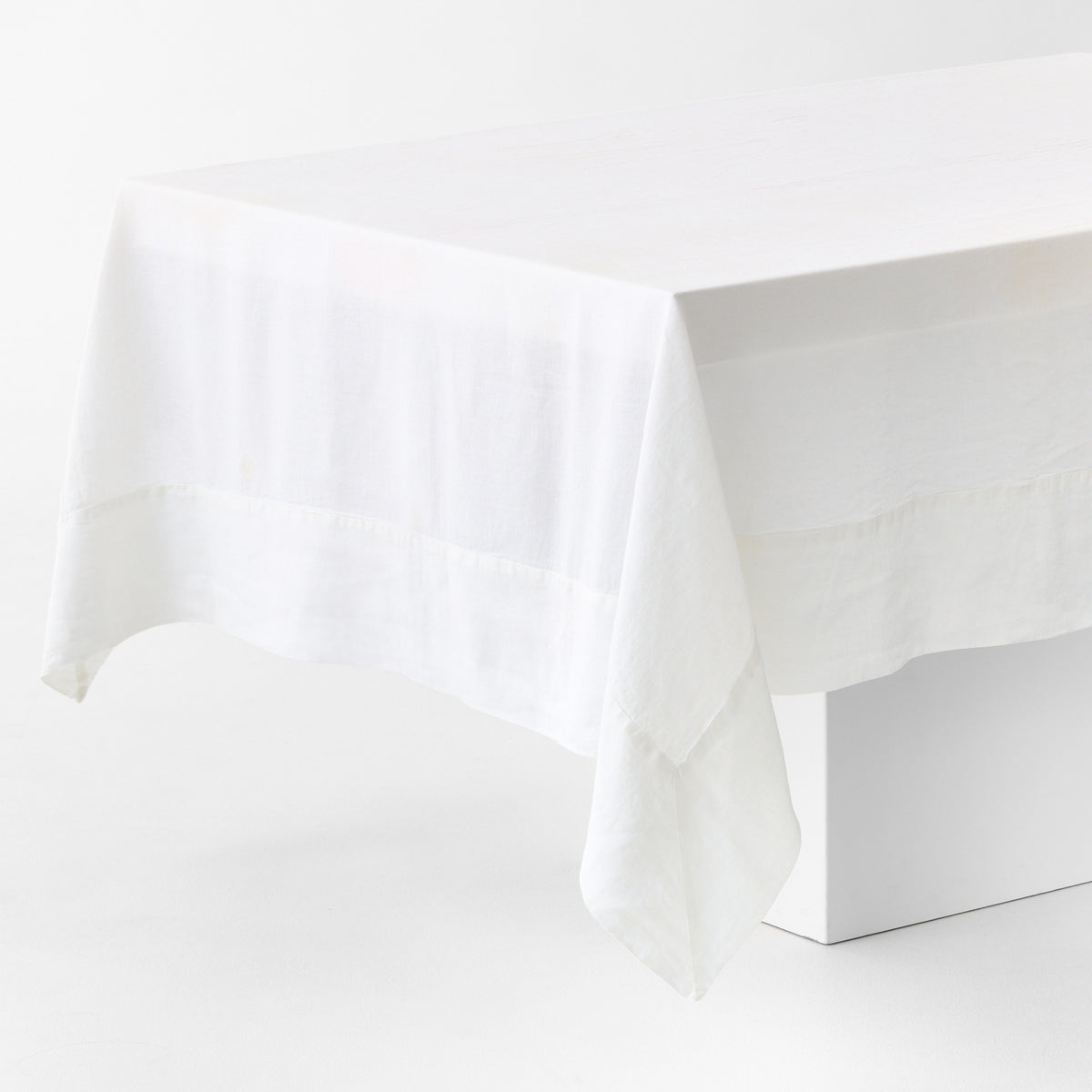 White hand-dyed 100% linen tablecloth with a wide border and mitered corner detailing draped over a table.