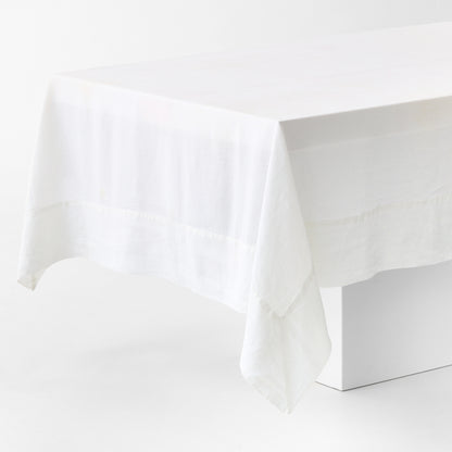 White hand-dyed 100% linen tablecloth with a wide border and mitered corner detailing draped over a table.