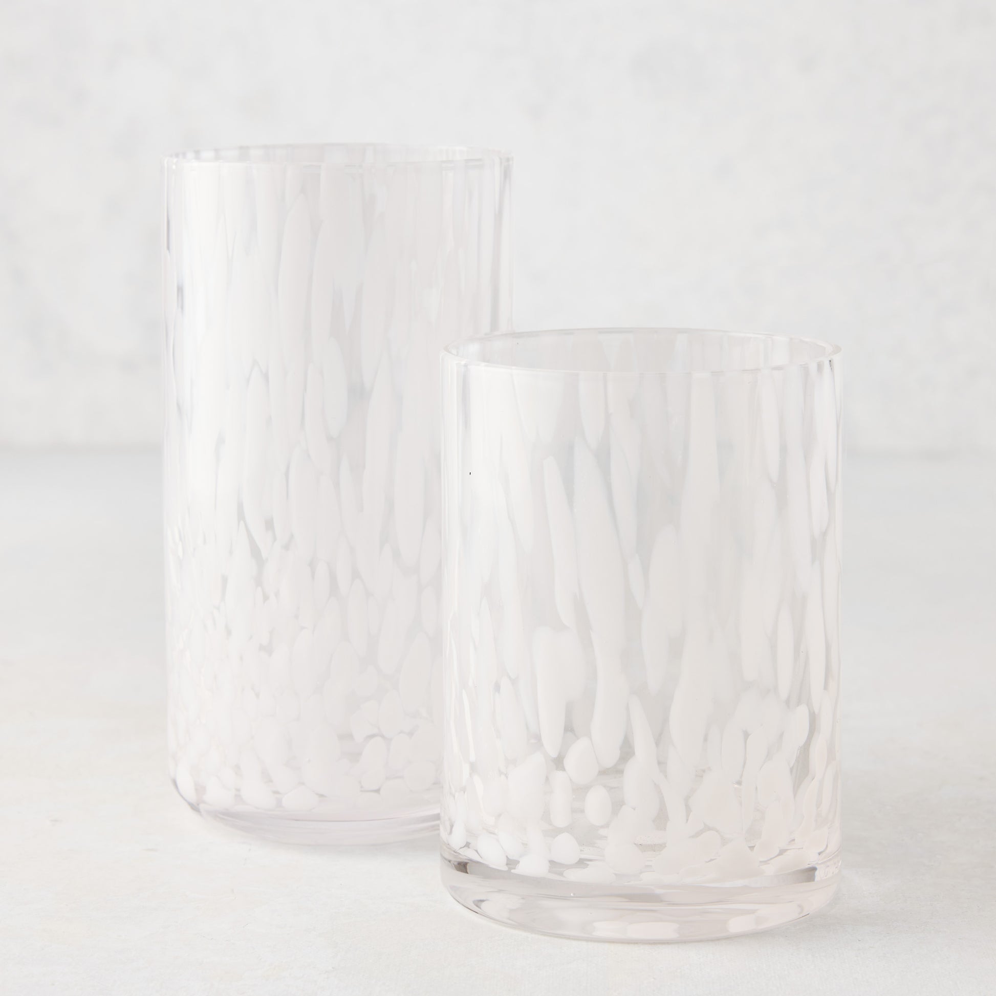 Two clear glass highball glasses with white spotted patterns, one taller than the other.