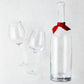 Clear glass wine carafe with red ribbon and two large wine glasses.