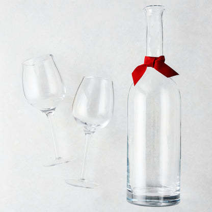 Clear glass wine carafe with red ribbon and two large wine glasses.