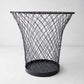 Black wire waste bin made of woven iron, 12"H, with a flared top and solid base.