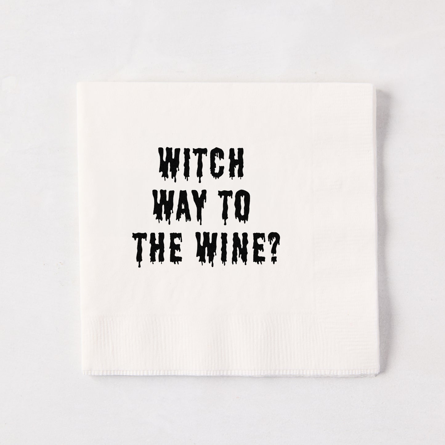 White 5.5-inch square 3-ply paper cocktail napkin with black dripping text reading Witch Way to the Wine.