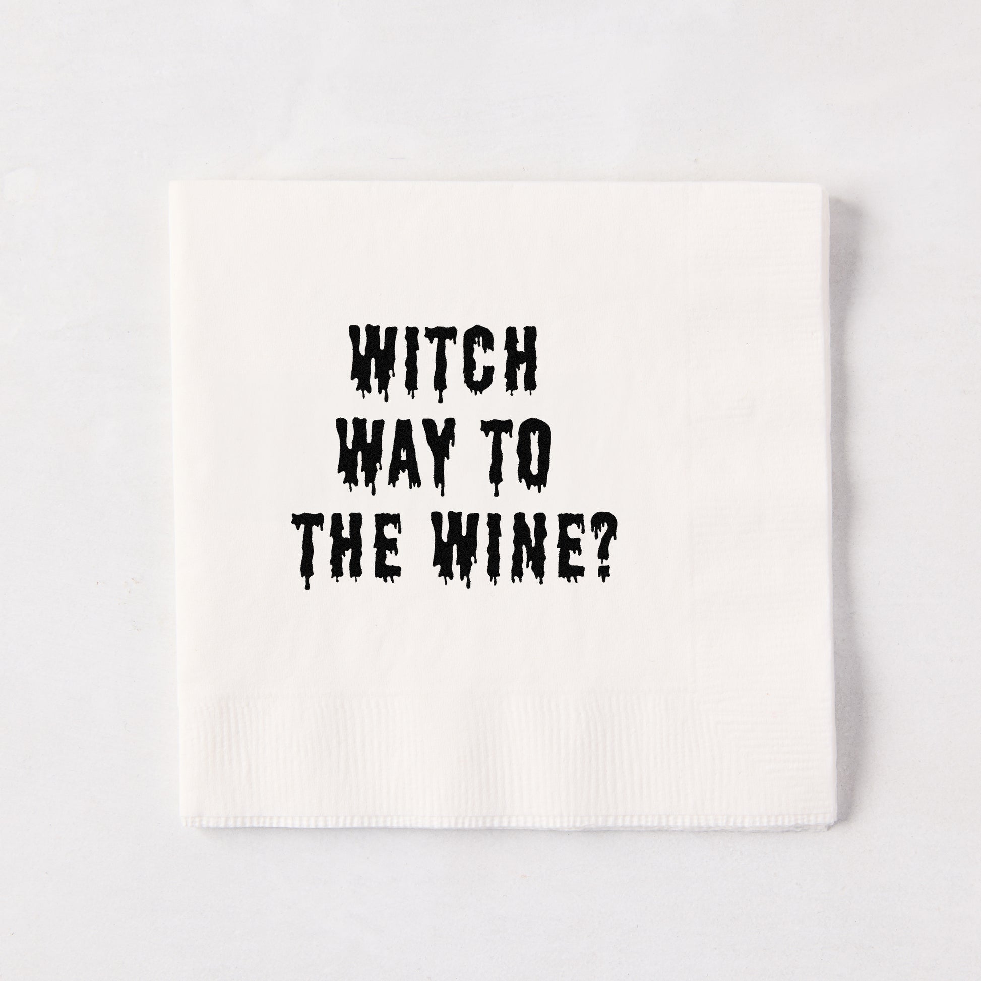 White 5.5-inch square 3-ply paper cocktail napkin with black dripping text reading Witch Way to the Wine.