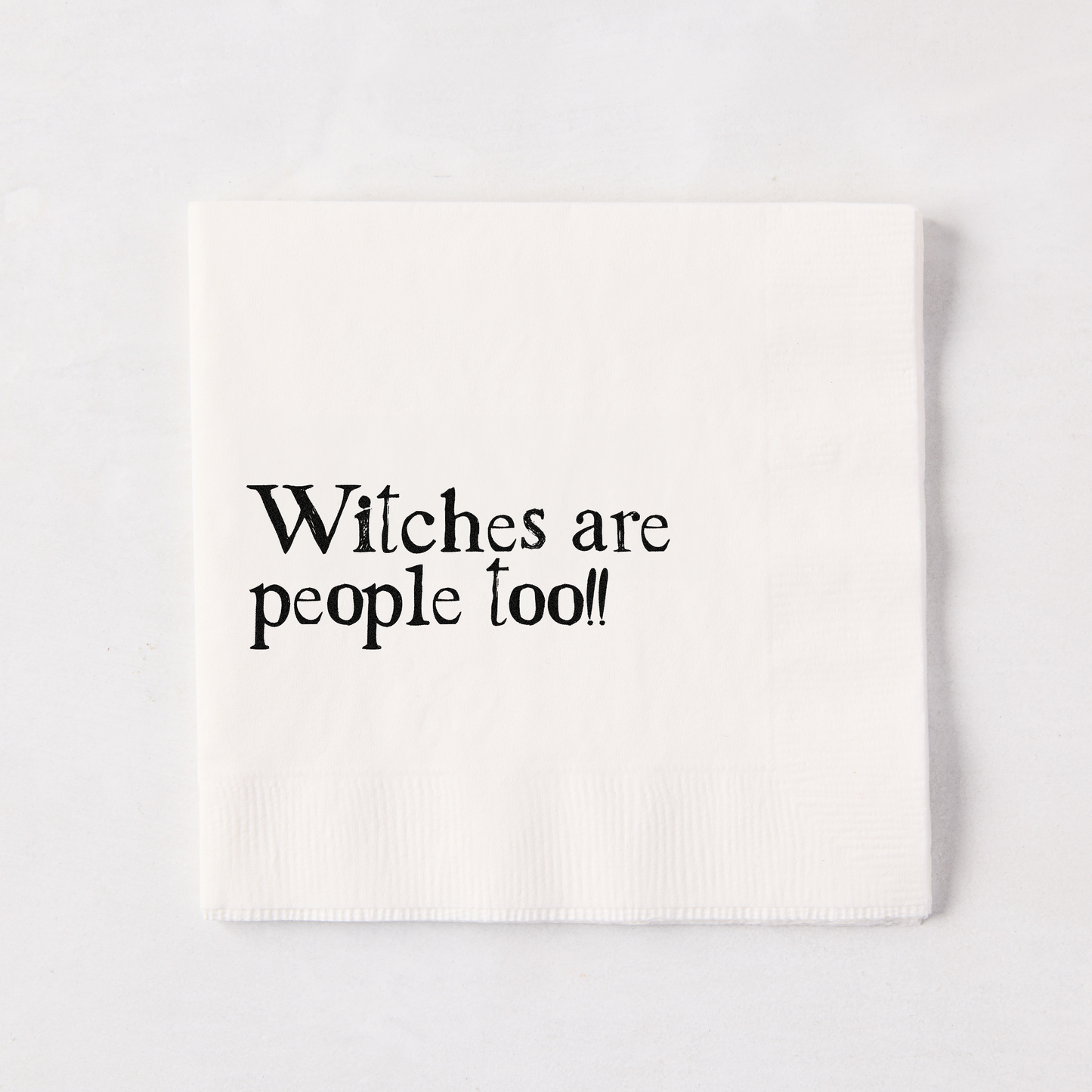 White 5.5" square paper napkin with "Witches are people too!!" in black text.