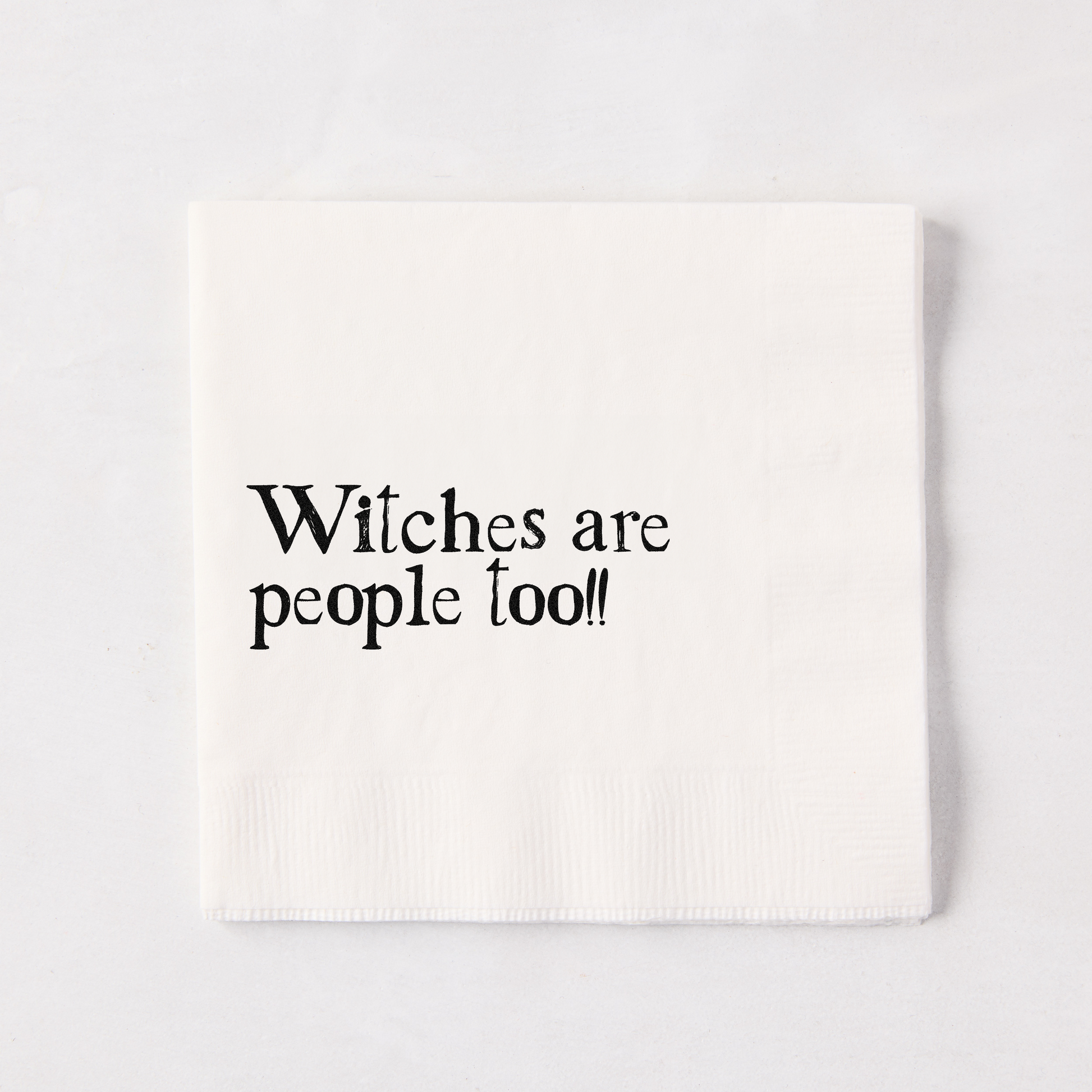 White 5.5" square paper napkin with "Witches are people too!!" in black text.