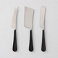Three-piece cheese knife set with stainless steel blades and black, hand-forged, hammered metal handles.